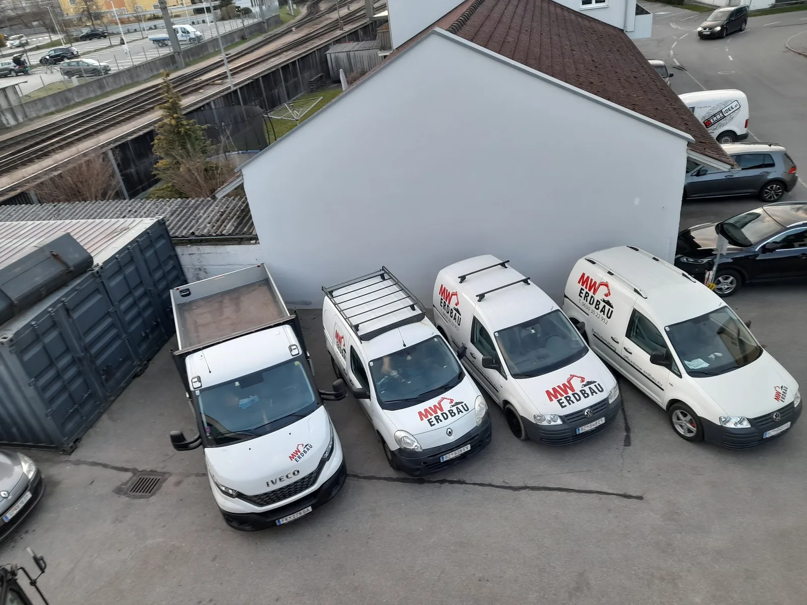 Vier beschriftete Fahrzeuge von MW Erdbau von oben fotografiert, eine Pritsche und drei Kastenwagen