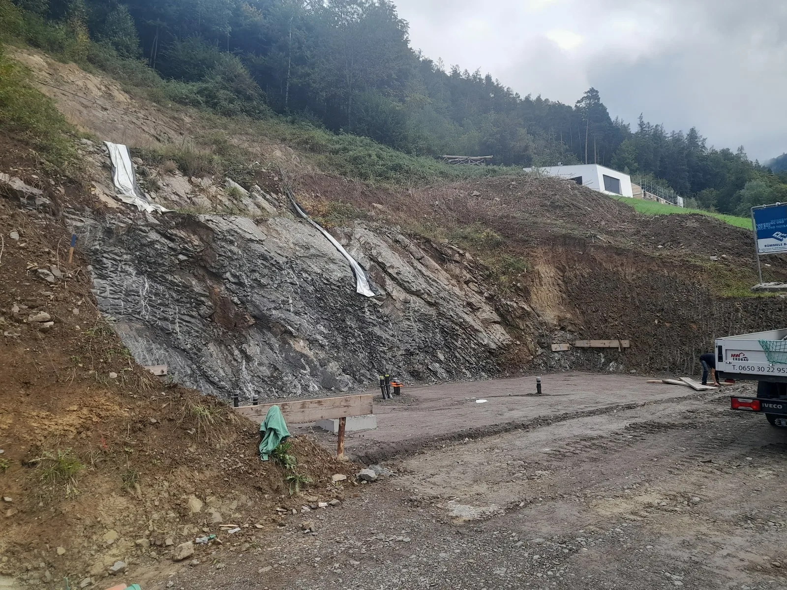 Freigelegte Felswand an einer Baustelle, davor eine planierte Fläche und ein Pritschenwagen von MW Erdbau
